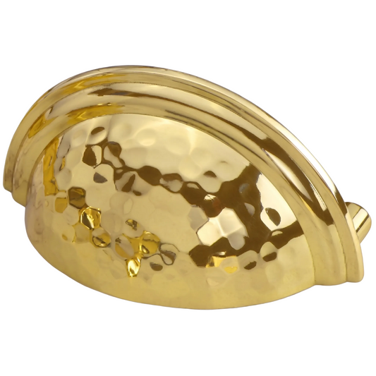 A polished gold metal cabinet pull handle with a hammered texture on the front and a smooth curved back, shown on a light marble surface.