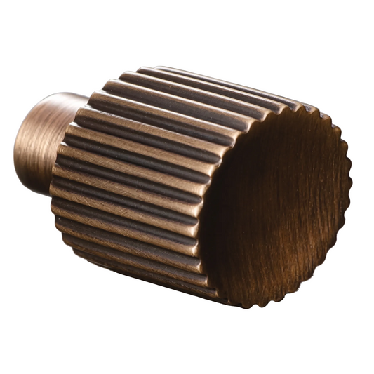 A close-up of a metallic gear-shaped hardware component with a brushed bronze finish, resting on a dark textured stone surface.