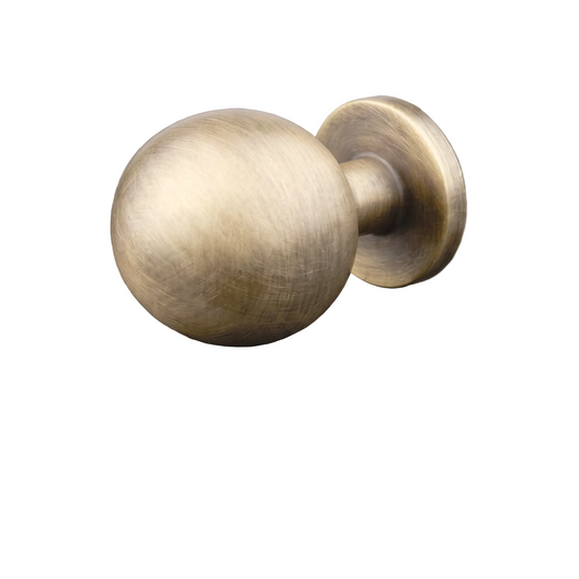 A single round cabinet knob with a brushed antique brass finish, resting on a dark gray reflective surface.