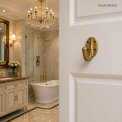 A close-up of a polished solid brass door pull handle mounted on a white paneled door, with a luxurious bathroom interior visible in the background featuring a marble tub, chandelier, and vanity.